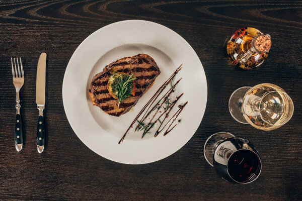 top view of beef steak on plate and glasses with wine on table