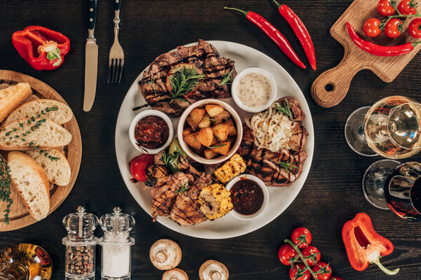 top view of plate with beef steaks, chicken wings and wine on table