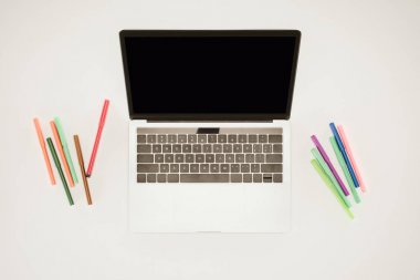 Laptop beyaz yüzey üzerinde renkli Keçeli Kalemler arasında boş ekran ile 