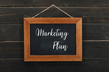 Board with lettering marketing plan hanging on wooden wall clipart