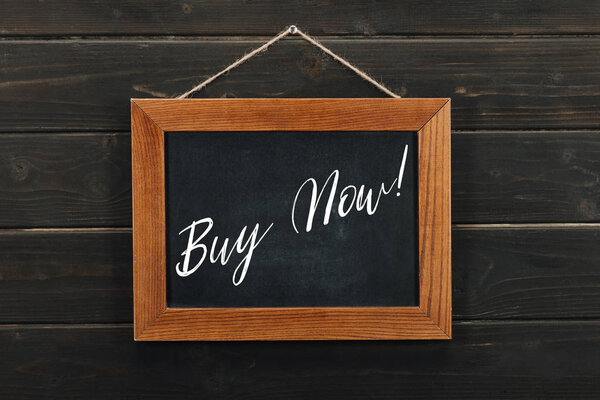 Доска с надписью купить теперь висит на деревянной стене
