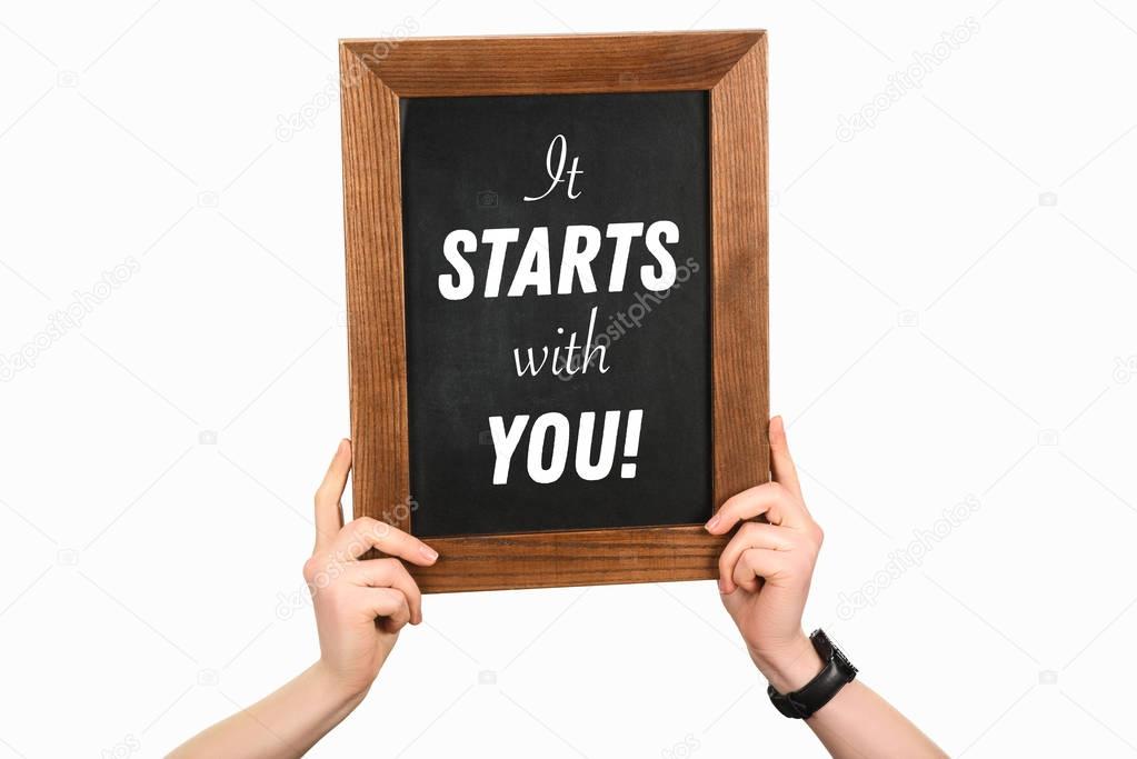 Cropped image of woman hands holding board with lettering it starts with you isolated on white