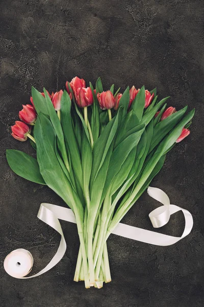 美丽的红色郁金香和丝带在黑暗的表面上的花束 — 图库照片