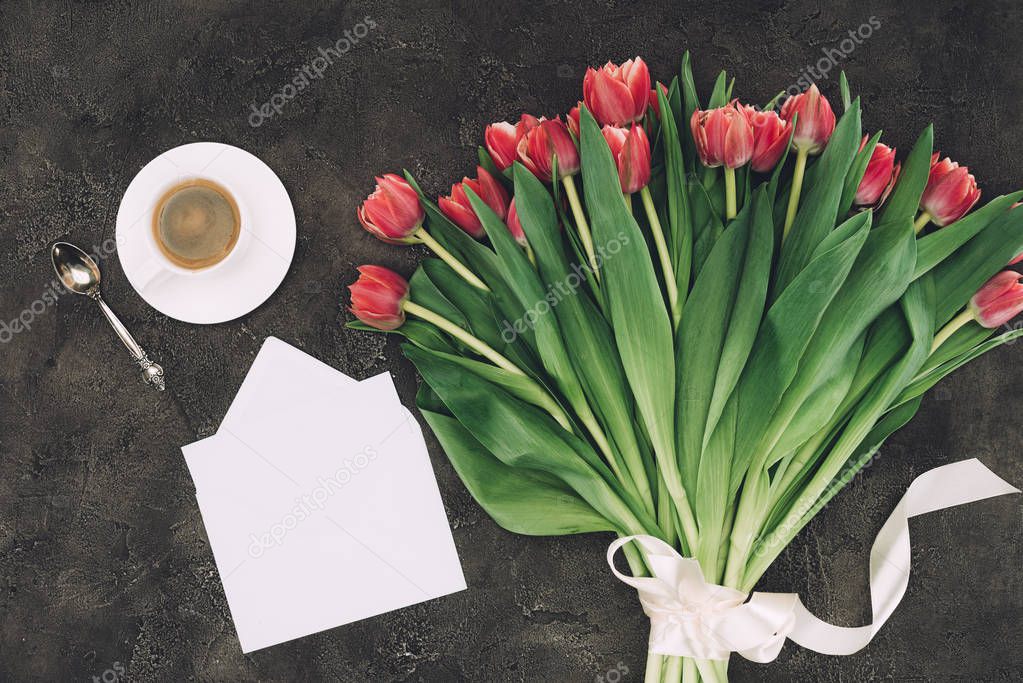 top view of beautiful red tulips, cup of coffee and blank envelope with greeting card