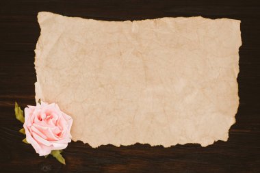 top view of blank aged paper and rose flower on wooden table clipart