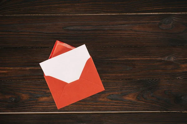 top view of red envelope with blank paper on wooden table