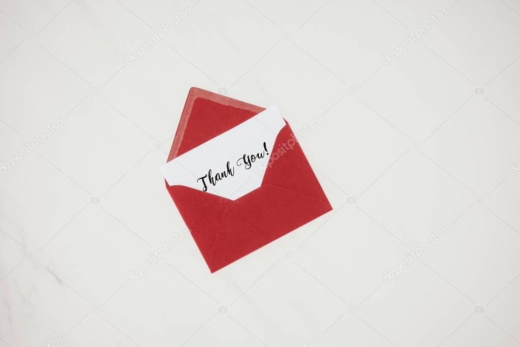 top view of red envelope with THANK YOU lettering on paper isolated on white