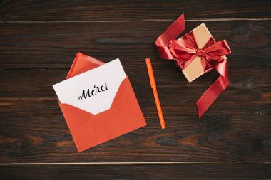 top view of red envelope with merci lettering on paper and gift box on wooden table clipart