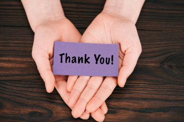 cropped shot of woman holding purple paper with thank you lettering over wooden table clipart