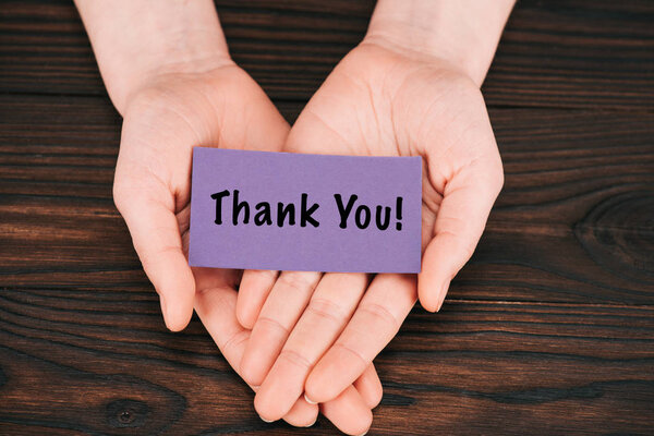 cropped shot of woman holding purple paper with thank you lettering over wooden table