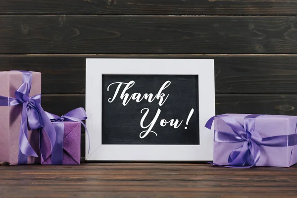 thank you lettering on blackboard in frame with gift boxes against wooden wall