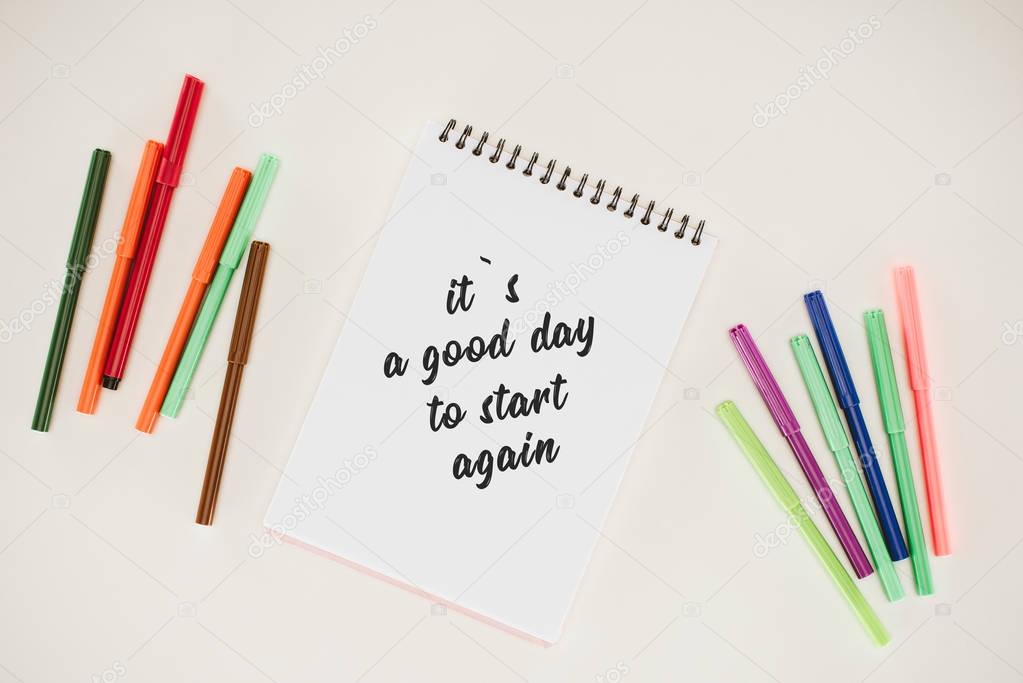 top view of notepad with its a good day to start again lettering and colorful markers isolated on white