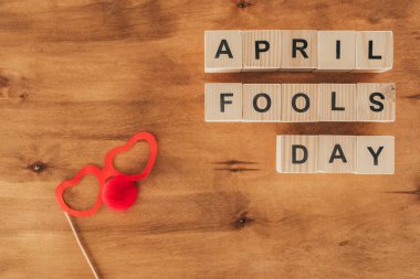top view of arranged wooden cubes in april fools day lettering with party eyeglasses and clown nose on wooden tabletop, 1 april holiday concept clipart