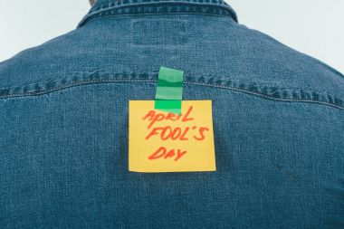 back view of man with note on sticky tape with april fools day lettering on back, april fools day holiday concept clipart