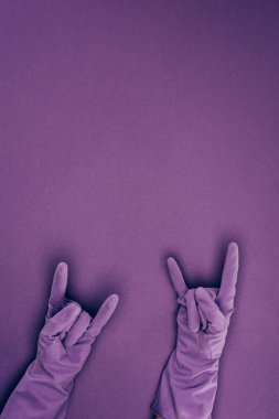 cropped image of woman showing rock signs in rubber protective gloves isolated on violet clipart