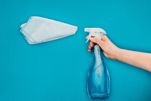 cropped image of woman holding spray bottle near rag isolated on blue