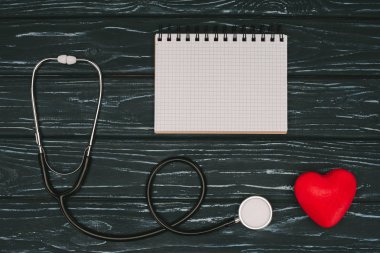 flat lay with arranged red heart, stethoscope and empty notebook on dark wooden tabletop, world health day concept clipart