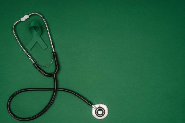 Yeşil farkındalık şerit üstten görünüm skolyoz, ruh sağlığı sembolü ve yeşil yüzey üzerinde izole stetoskop
