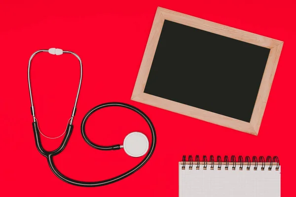 Draufsicht Auf Leere Tafel Notizbuch Und Stethoskop Isoliert Auf Roter — kostenloses Stockfoto