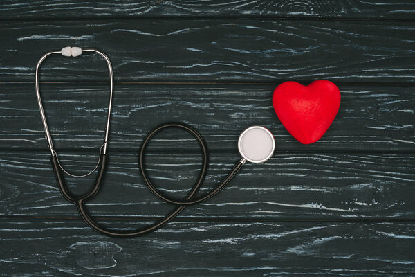 flat lay with red heart and stethoscope on dark wooden tabletop, world health day concept
