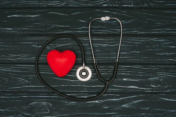 平躺与红色心脏和听诊器在黑暗的木桌上 世界卫生日概念 — 图库照片