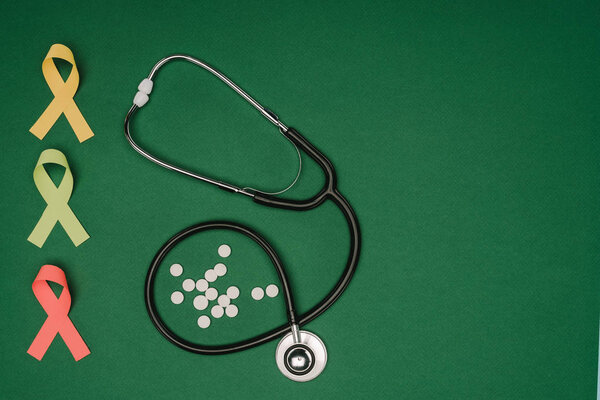 flat lay with arranged pills, colorful ribbons and stethoscope isolated on green tabletop, world health day concept