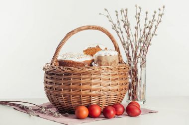 basket with easter cakes, painted eggs and catkins on grey  clipart