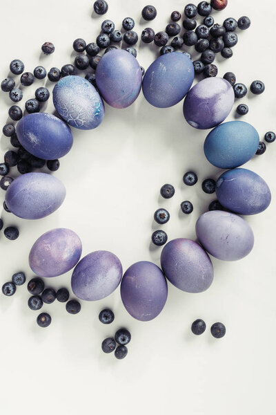 circle made from violet painted easter eggs and blueberries on grey
