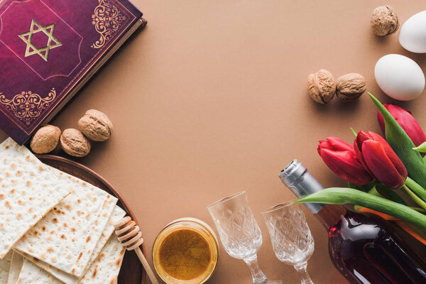 top view of traditional book with text in hebrew, honey and matza on brown table