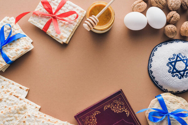 top view of traditional book with text in hebrew, kippah and matza on brown table