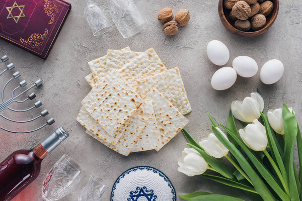 top view of traditional book with text in hebrew, matza and menorah on concrete table