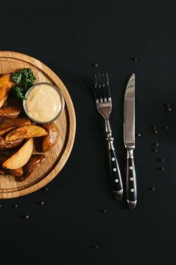 soslu fırında patates üstten görünüm ahşap tahta ve çatal bıçak siyah ile