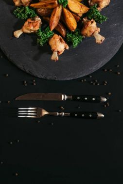 top view of tasty roasted potatoes with chicken and fork with knife on black clipart