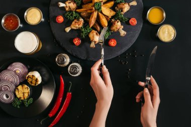çatal ve bıçak tutarak ve siyahta lezzetli fırında patates kızarmış tavuk ve sebze yeme kişi resmini kırpılmış