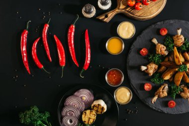 top view of red peppers, sauces, vegetables and tasty baked potatoes with roasted chicken on black clipart