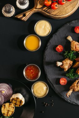 top view of tasty roasted chicken wings with various sauces and vegetables on black clipart