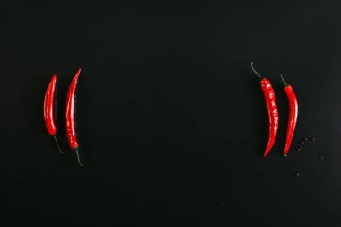 top view of red chili peppers and peppercorns on black background