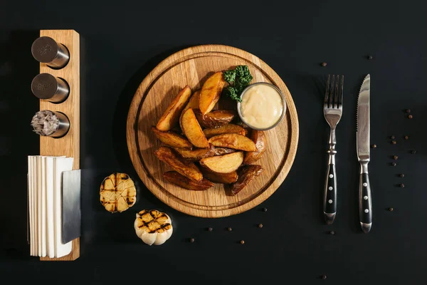木の板 焼きにんにく 黒のナイフとフォークにおいしいロースト ポテト ソースのトップ ビュー — ストック写真