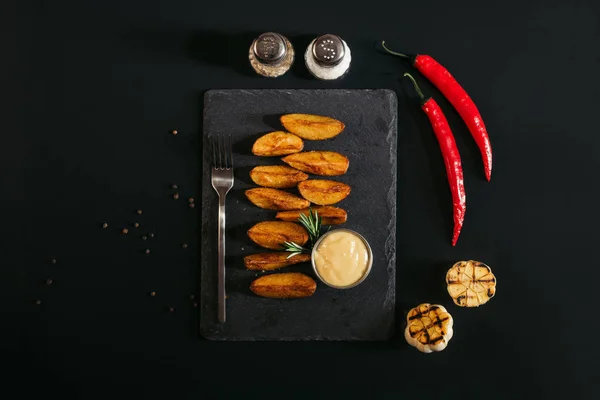 在石板板和香料与大蒜和辣椒辣椒在黑色的美味烤土豆的顶级视图 — 图库照片