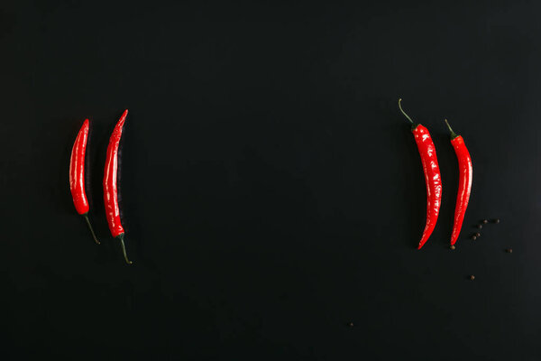 top view of red chili peppers and peppercorns on black background