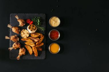 top view of tasty baked potatoes with grilled garlic and chicken, herbs and sauces on black clipart