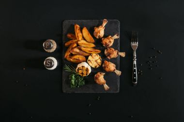top view of delicious roasted potatoes with chicken and grilled garlic on slate board on black  clipart