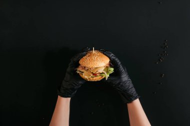kırpılan Türkiye, sebze ve Sezar sos ile lezzetli burger siyah üzerine tutarak eldiven elinde kadeh