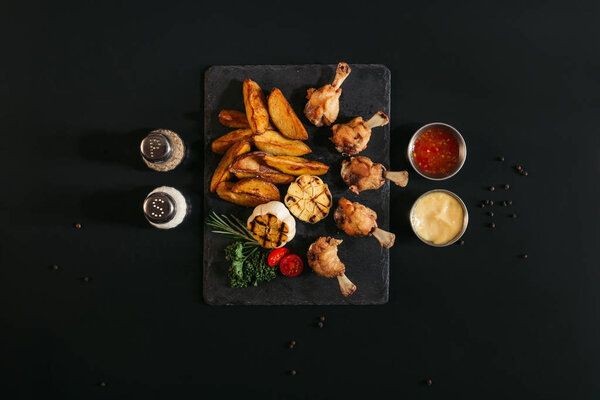 delicious roasted potatoes with chicken and grilled garlic on slate board with spices and sauces on black 