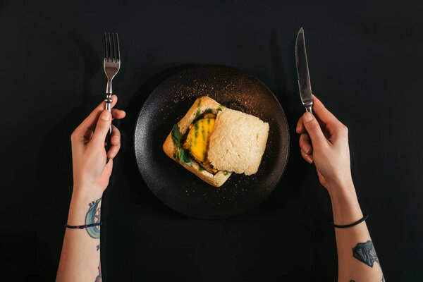top view of person holding fork and knife while eating delicious vegan burger on black