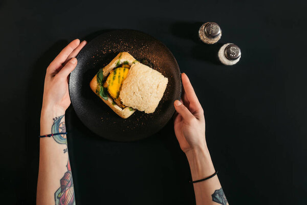 partial top view of person eating delicious vegan burger on black