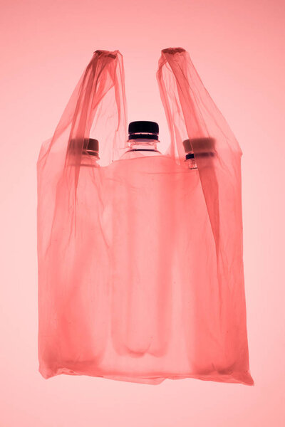 transparent plastic bag with plastic bottles under pastel pink toned light