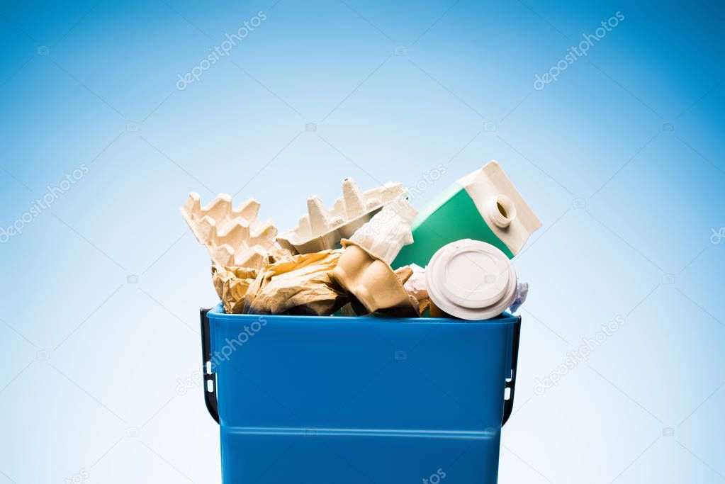 various paper trash in trash bin on blue