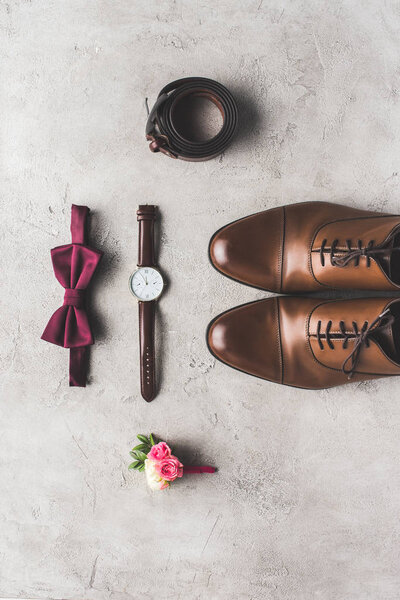 top view of wedding bow tie, boutonniere, wristwatch and shoes for groom on gray surface