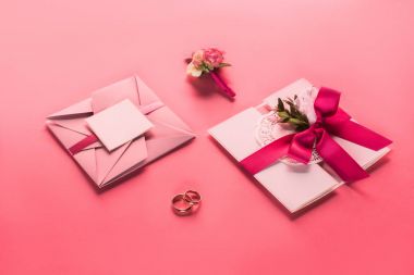 wedding rings, boutonniere and pink envelopes with invitations on pink surface clipart